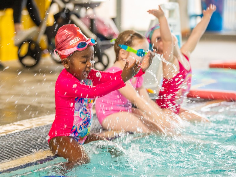 Children in colorful swimsuits playing and splashing in an indoor pool, enjoying a fun day of swimming together.