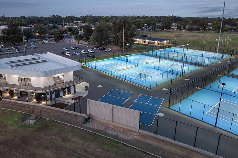 an Aerial shot of the Jim Elphick Tennis Centre on dusk with the lights on.